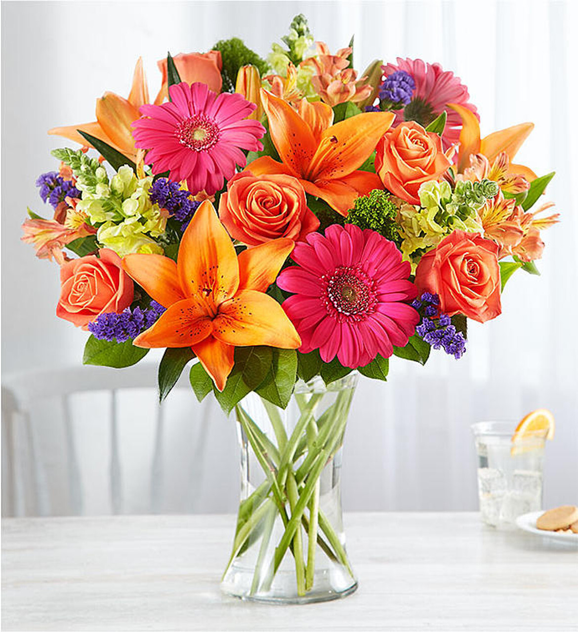 Bright floral arrangement featuring orange lilies, coral roses, and pink daisies in a glass vase—perfect for every occasion.