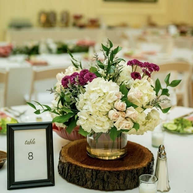Wedding centerpiece of white hydrangeas, blush roses, snapdragons, eucalyptus, and berries in a glass vase.