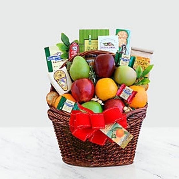 Gift basket filled with assorted fruits, snacks, and cheese, topped with a large red bow and gift tag.