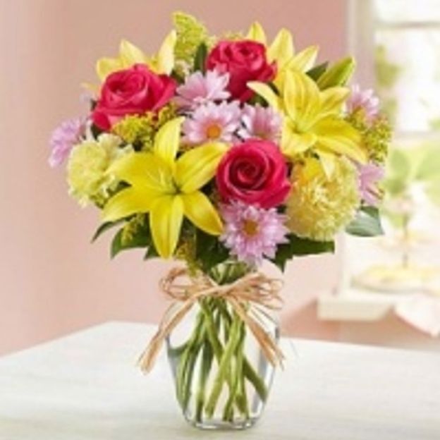 Lilies, roses, carnations, daisies, solidago, and greens arranged in a clear glass vase—mixed colors, balanced shape, and easy to place.