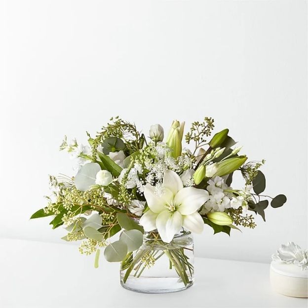White daisies, yellow roses, green Athos poms, and yellow alstroemeria styled in a clear bubble bowl—neat scale for desks or side tables.