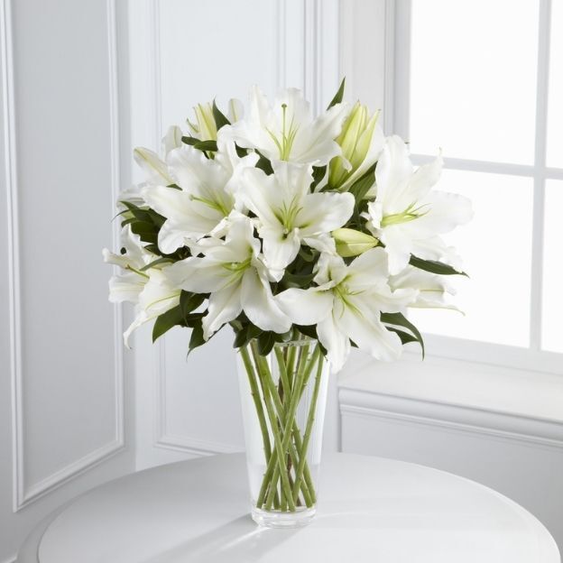 Oriental lilies arranged with lush greens in a clear glass vase.